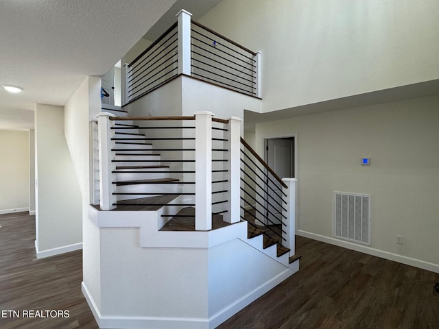 staircase with hardwood / wood-style flooring, a towering ceiling, and a textured ceiling