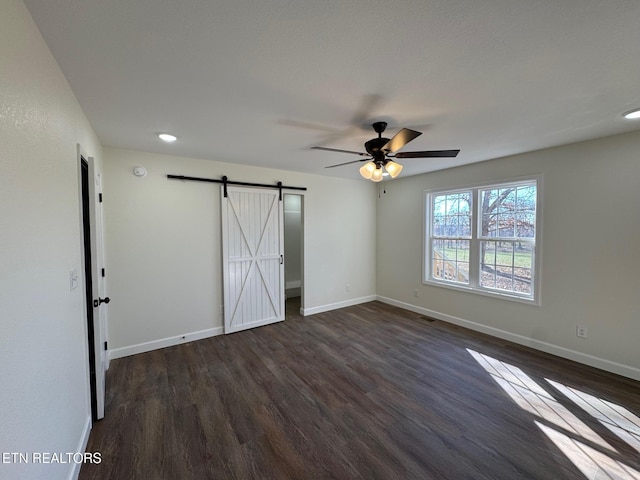 unfurnished bedroom featuring dark hardwood / wood-style floors, ceiling fan, and a barn door