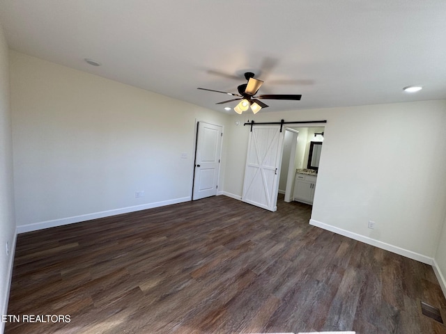 unfurnished bedroom featuring ceiling fan, a barn door, and dark hardwood / wood-style flooring