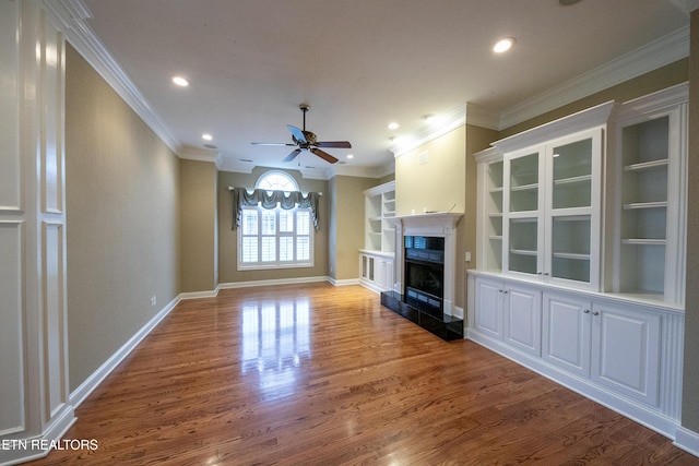 unfurnished living room featuring built in shelves, wood-type flooring, and ornamental molding