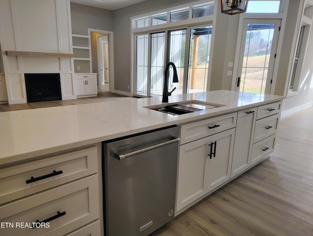 kitchen featuring light wood-type flooring, white cabinets, light stone counters, sink, and dishwasher