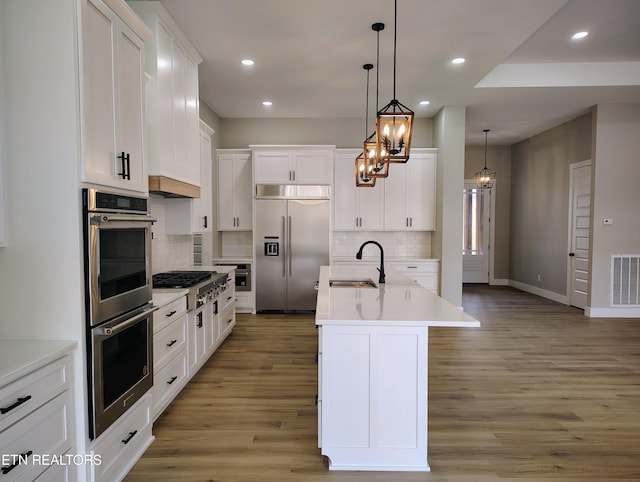 kitchen with a kitchen island with sink, hanging light fixtures, sink, white cabinetry, and stainless steel appliances