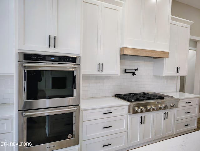 kitchen with white cabinets, appliances with stainless steel finishes, backsplash, and light stone countertops