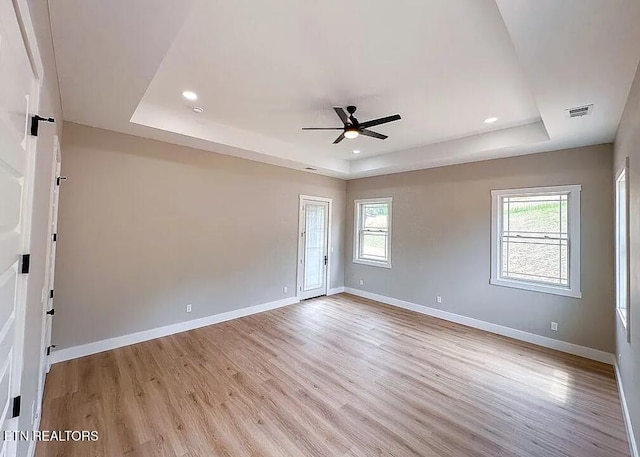 unfurnished room with light wood-type flooring, a raised ceiling, and ceiling fan