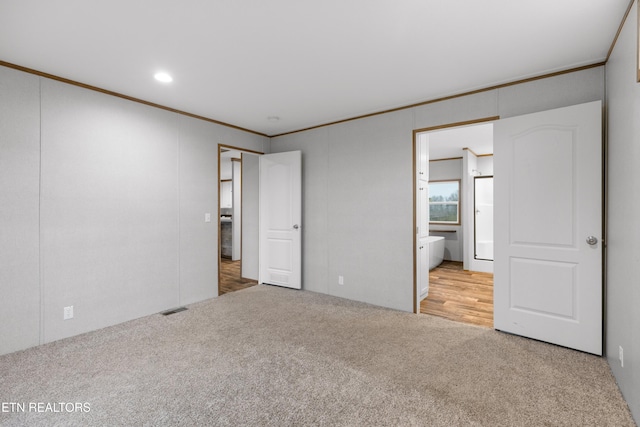 unfurnished bedroom with light colored carpet, ensuite bath, and ornamental molding