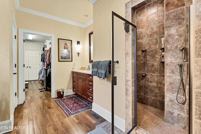 bathroom with hardwood / wood-style flooring, ornamental molding, tiled shower, and vanity