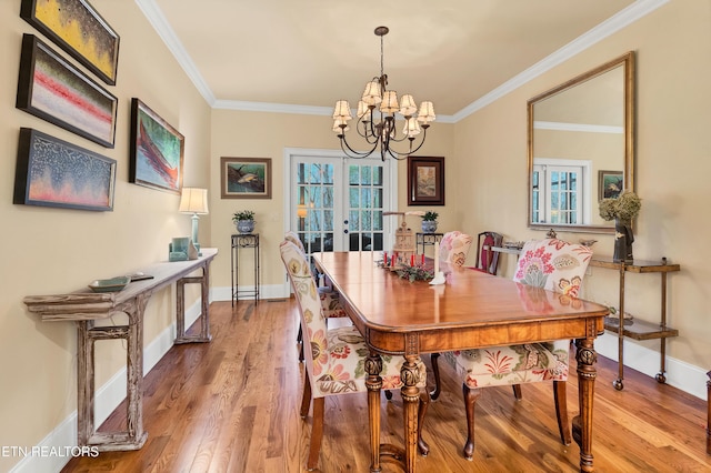 dining area with hardwood / wood-style flooring, crown molding, an inviting chandelier, and french doors