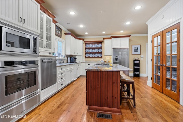 kitchen featuring a kitchen island, appliances with stainless steel finishes, a breakfast bar area, white cabinets, and light stone countertops