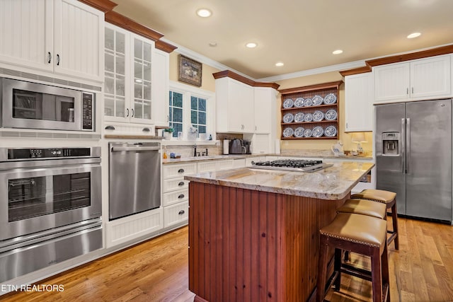 kitchen featuring stainless steel appliances, light stone counters, ornamental molding, white cabinets, and light wood-type flooring