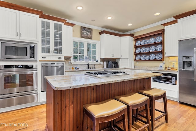 kitchen featuring appliances with stainless steel finishes, tasteful backsplash, white cabinets, light stone countertops, and light wood-type flooring