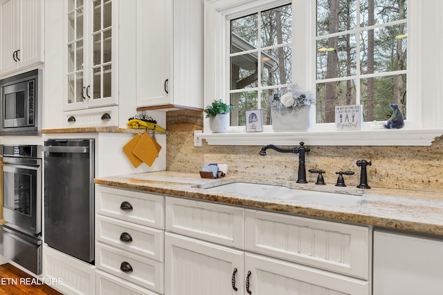 kitchen featuring appliances with stainless steel finishes, white cabinetry, sink, backsplash, and light stone countertops