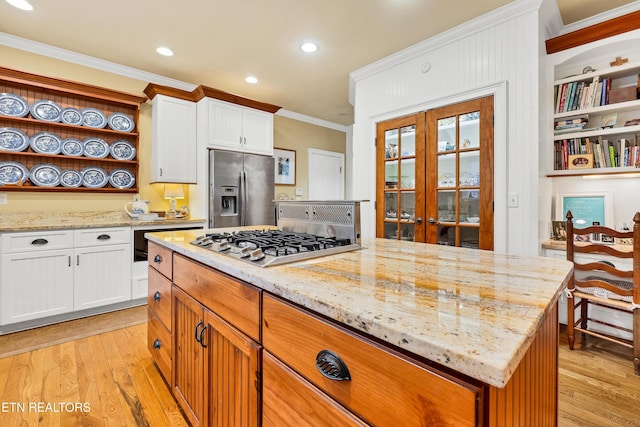 kitchen featuring stainless steel appliances, light stone counters, ornamental molding, white cabinets, and light wood-type flooring