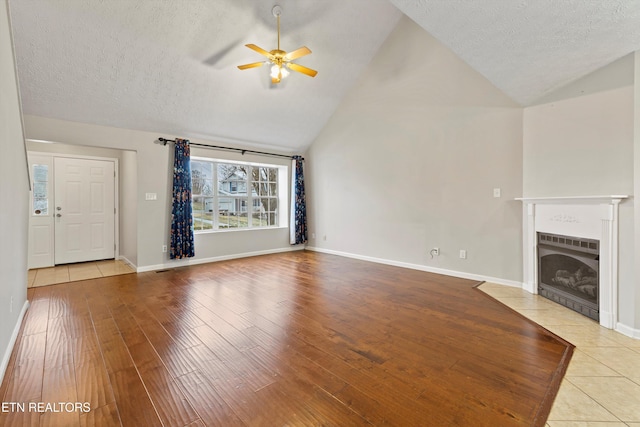 unfurnished living room featuring a fireplace, high vaulted ceiling, ceiling fan, and light hardwood / wood-style flooring