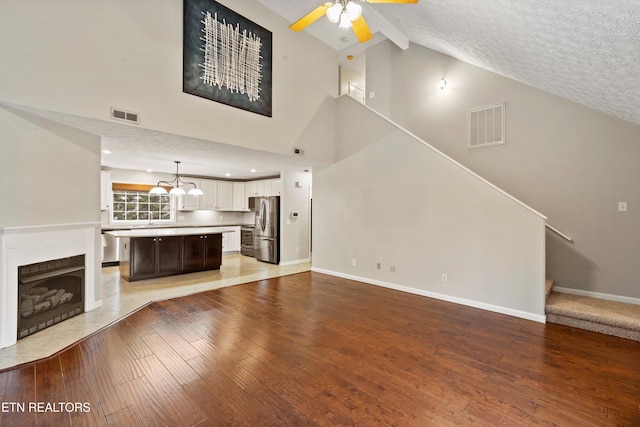 unfurnished living room featuring high vaulted ceiling, a textured ceiling, ceiling fan, and hardwood / wood-style floors