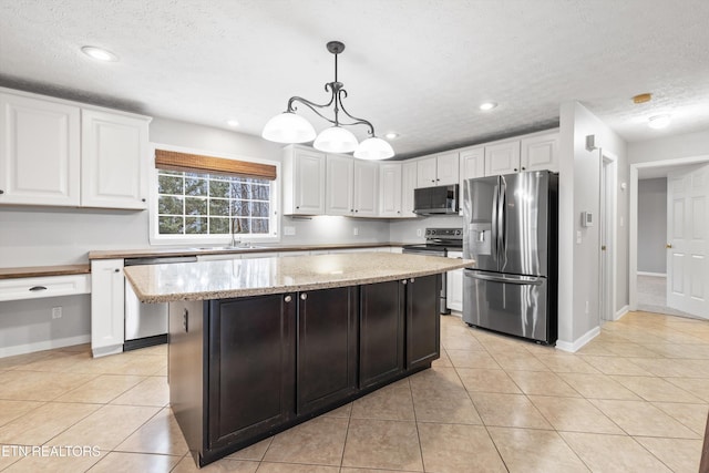 kitchen with stainless steel appliances, hanging light fixtures, a center island, light stone counters, and white cabinets