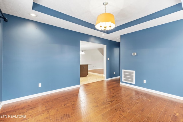 unfurnished room with hardwood / wood-style flooring, a notable chandelier, and a tray ceiling