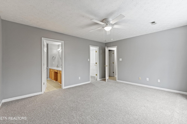 unfurnished bedroom featuring light colored carpet, ceiling fan, a textured ceiling, sink, and ensuite bathroom