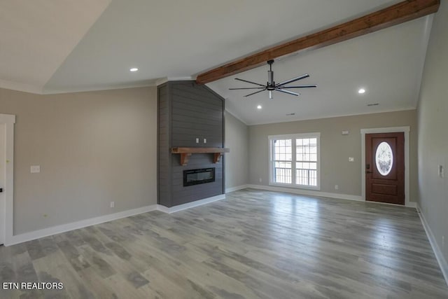 unfurnished living room featuring ceiling fan, a large fireplace, lofted ceiling with beams, and light hardwood / wood-style flooring