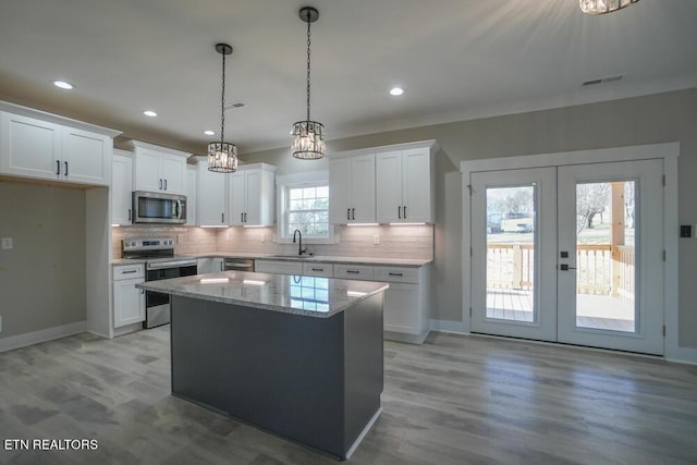 kitchen with white cabinetry, french doors, light stone countertops, a kitchen island, and appliances with stainless steel finishes