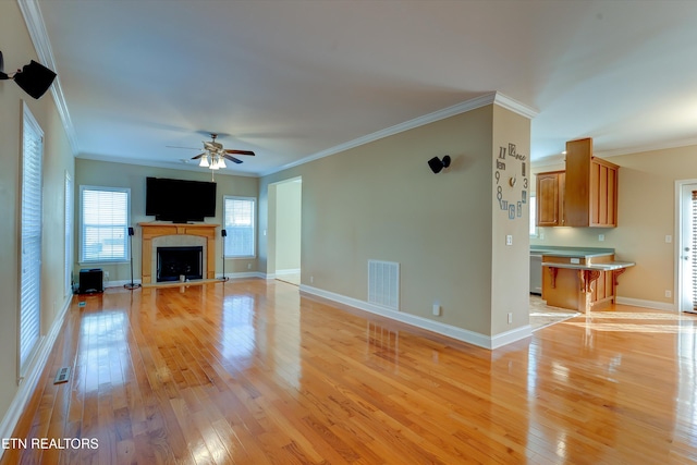 unfurnished living room featuring a tiled fireplace, crown molding, ceiling fan, and light wood-type flooring