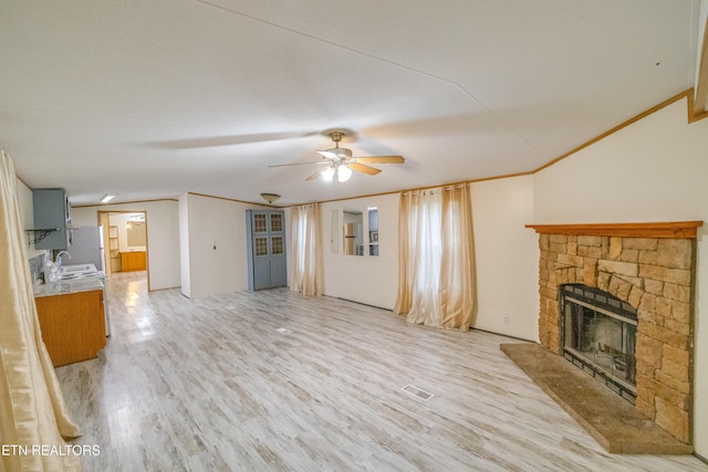 unfurnished living room featuring light wood-type flooring, ceiling fan, crown molding, sink, and a fireplace