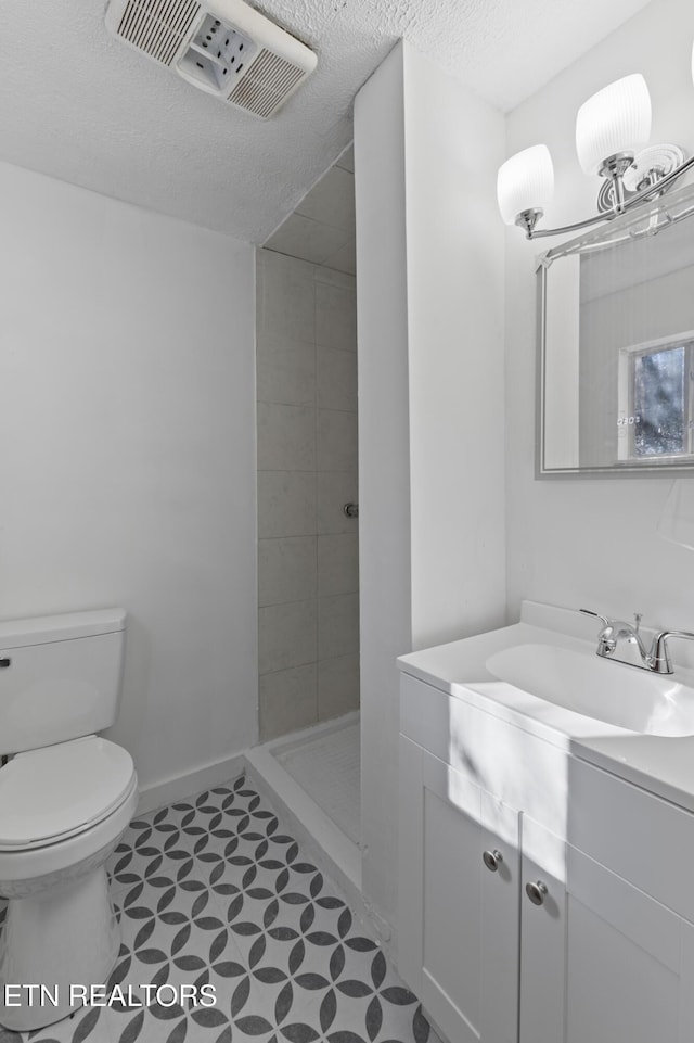 bathroom featuring a tile shower, vanity, a textured ceiling, and toilet