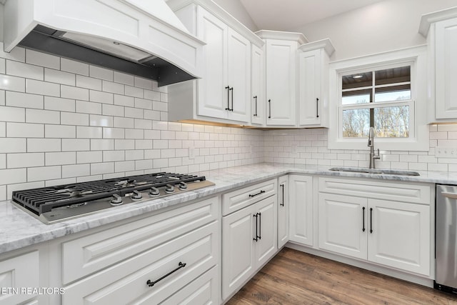 kitchen with custom exhaust hood, stainless steel appliances, decorative backsplash, white cabinetry, and sink