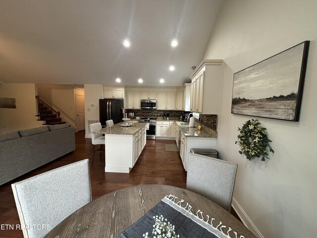 kitchen with a sink, a center island, open floor plan, appliances with stainless steel finishes, and light stone countertops