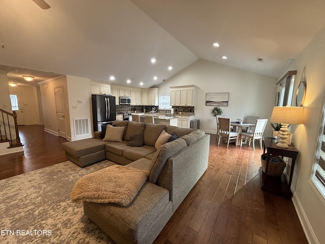 living area featuring lofted ceiling, dark wood-type flooring, visible vents, baseboards, and stairway