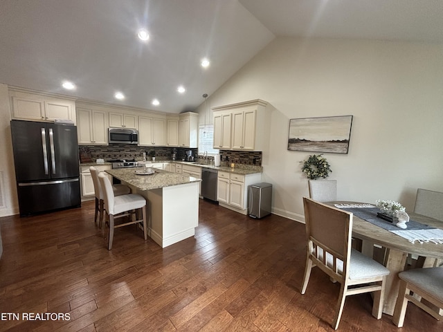 kitchen with appliances with stainless steel finishes, a center island, dark hardwood / wood-style flooring, tasteful backsplash, and light stone counters