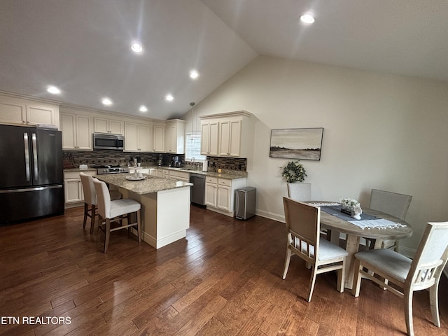 kitchen featuring appliances with stainless steel finishes, dark hardwood / wood-style floors, tasteful backsplash, a kitchen island, and light stone counters