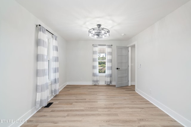 spare room featuring a chandelier and light wood-type flooring