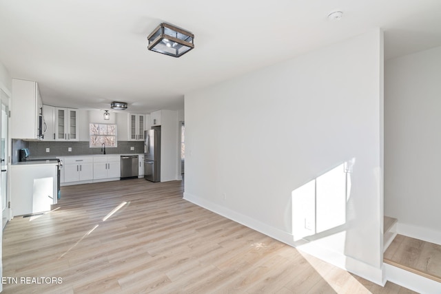 interior space featuring appliances with stainless steel finishes, tasteful backsplash, sink, light hardwood / wood-style flooring, and white cabinets