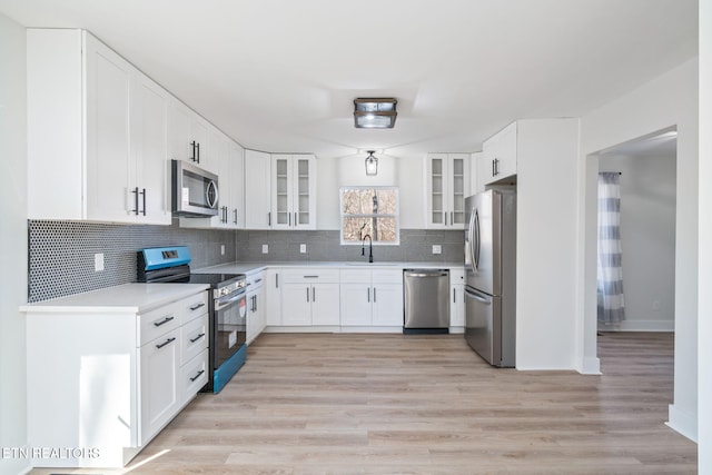 kitchen with light wood-type flooring, tasteful backsplash, stainless steel appliances, sink, and white cabinets