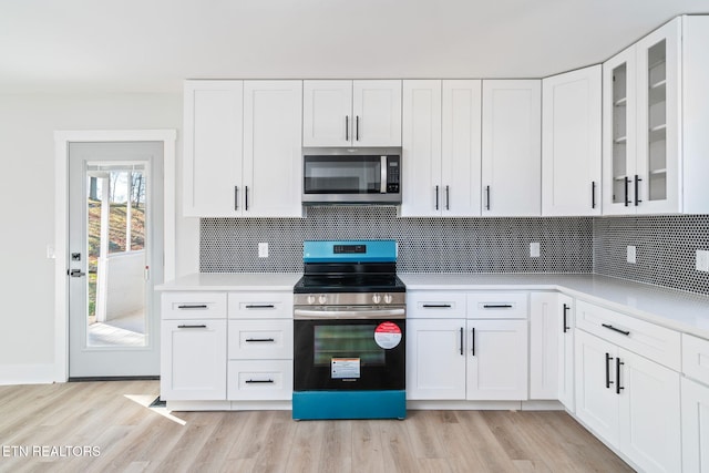 kitchen with light wood-type flooring, white cabinetry, appliances with stainless steel finishes, and tasteful backsplash