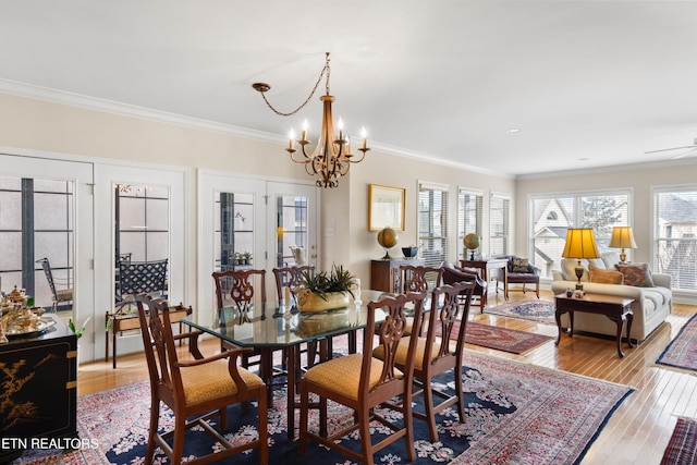 dining space with light wood finished floors, ornamental molding, a chandelier, and a wealth of natural light