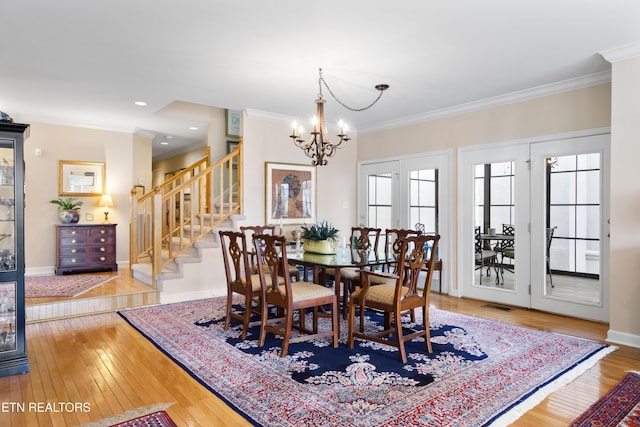 dining room with visible vents, an inviting chandelier, ornamental molding, hardwood / wood-style floors, and stairs