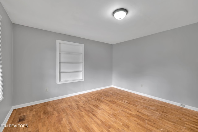 unfurnished room featuring built in features and hardwood / wood-style flooring