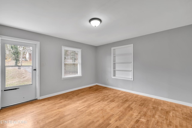 unfurnished room featuring built in shelves and light hardwood / wood-style floors