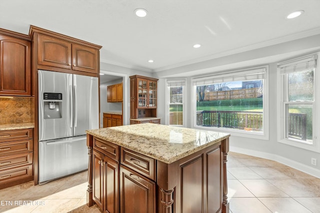 kitchen featuring stainless steel fridge, light stone counters, crown molding, a kitchen island, and light tile patterned flooring