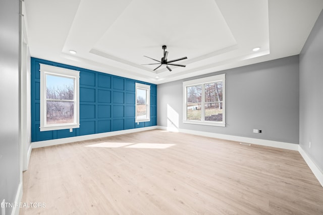 empty room featuring a raised ceiling, ceiling fan, and light hardwood / wood-style floors