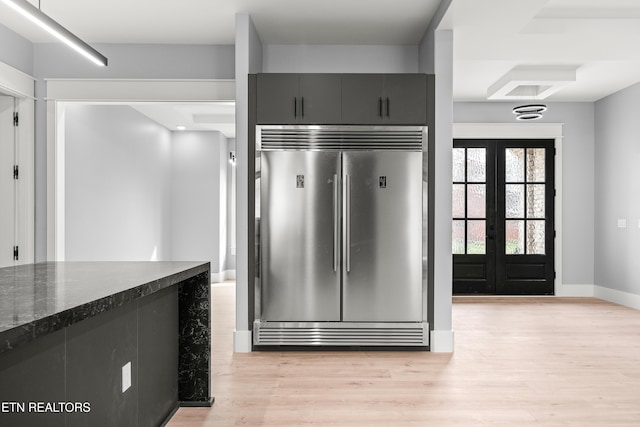 kitchen featuring dark stone countertops, built in refrigerator, french doors, and light hardwood / wood-style flooring