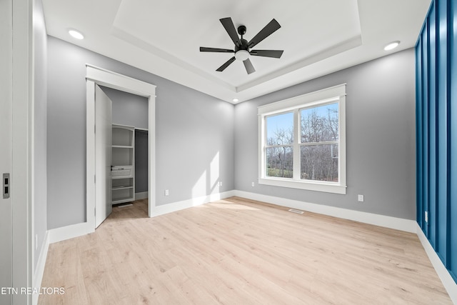 unfurnished bedroom with a raised ceiling, ceiling fan, a spacious closet, light hardwood / wood-style floors, and a closet