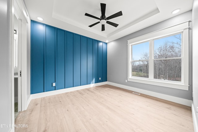 spare room with ceiling fan, light hardwood / wood-style floors, and a raised ceiling