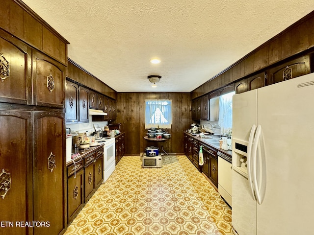 kitchen with wood walls, dark brown cabinetry, white appliances, and a textured ceiling