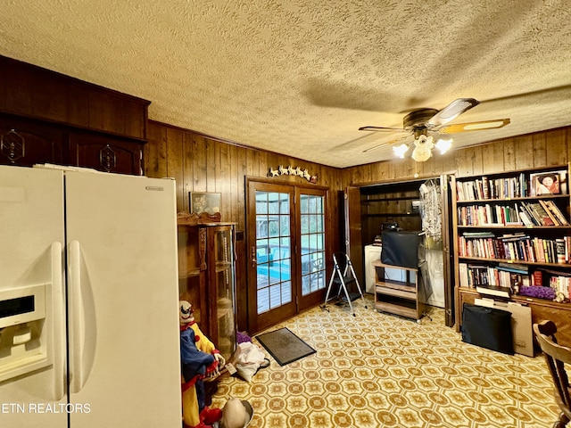 living area featuring ceiling fan, a textured ceiling, wood walls, and french doors