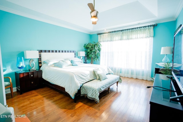 bedroom featuring hardwood / wood-style floors, crown molding, a raised ceiling, and ceiling fan