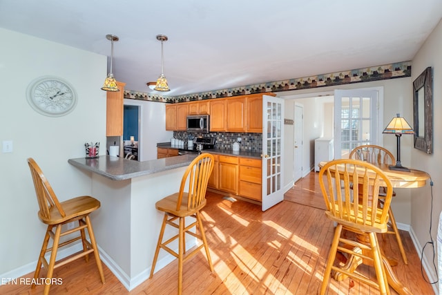 kitchen featuring a kitchen bar, decorative backsplash, light wood-type flooring, stainless steel appliances, and washer / dryer