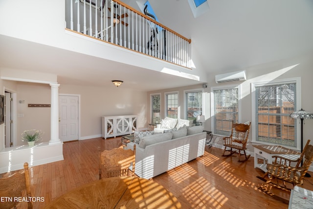 living room with a wall mounted air conditioner, wood-type flooring, high vaulted ceiling, and decorative columns