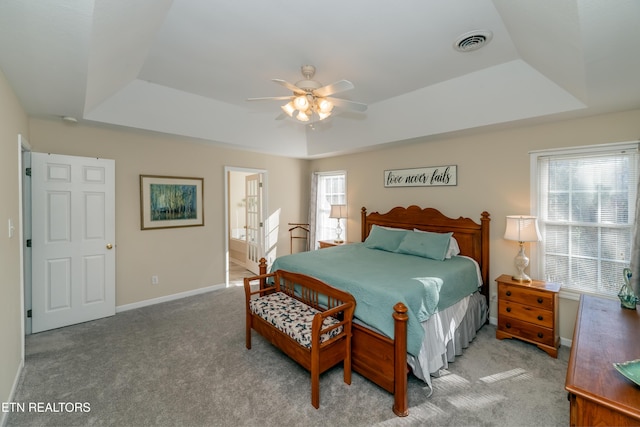 carpeted bedroom with multiple windows, a raised ceiling, and ceiling fan